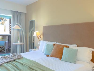 Habitación de hotel moderna con cama grande, cojines pastel y balcón.