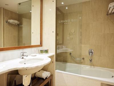 Baño iluminado con lavabo blanco, bañera y espejo grande.