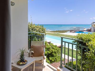 Balcón con silla y mesa, con vista a la piscina, áreas verdes y el mar al fondo.