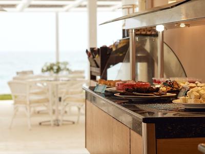 Buffet con varios platos en un restaurante luminoso con vista al mar.