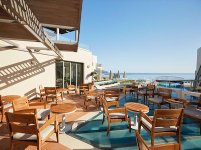 Terraza con mesas y sillas de madera, vista al mar y luz solar en el hotel.