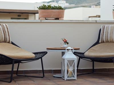 Dos sillas modernas con cojines en una terraza junto a una mesa pequeña y una linterna blanca.