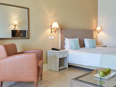 Habitación de hotel moderna con cama doble, mesita de noche y sillón en tonos cálidos.