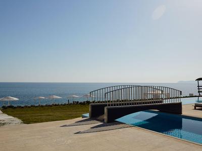 Piscina moderna con puente y vista al mar bajo un cielo despejado.