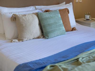 Cama bien hecha con sábanas blancas y varias almohadas decorativas en una habitación de hotel.