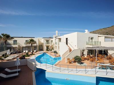 Complejo hotelero moderno con fachada blanca, piscina y tumbonas bajo un cielo azul claro.