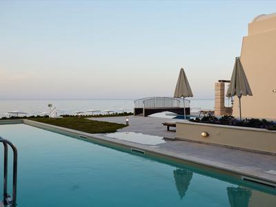 Piscina moderna de hotel con sombrillas y vista al mar al atardecer.