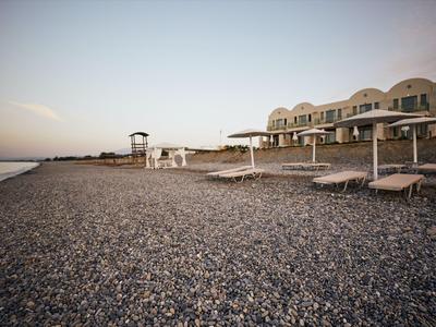 Playa de guijarros vacía con sombrillas y tumbonas frente a un hotel al anochecer.