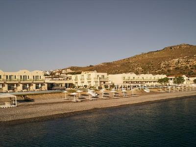 Complejo hotelero en la playa con sombrillas y montaña al fondo bajo cielo despejado.
