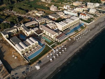 Vista aérea de un hotel frente a la playa con piscinas y tumbonas en la playa de arena.