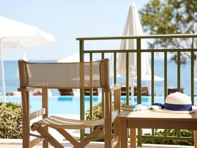 Una silla y mesa de madera con un sombrero, piscina y vista al mar al fondo.