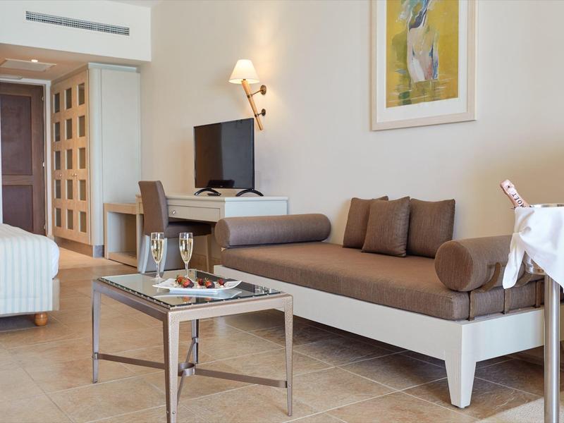 Area della camera d'hotel moderna con divano, TV, letto e piccolo tavolo con vino e snack.