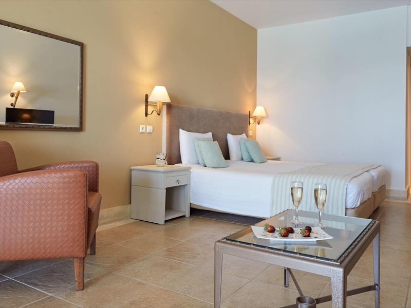 Camera d'hotel moderna con letto matrimoniale, poltrona, comodino e champagne sul tavolo.