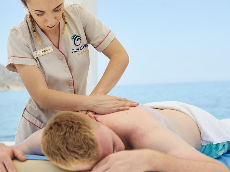 Massaggiatore che fa un massaggio alla schiena a una persona sulla spiaggia con cielo sereno e mare.