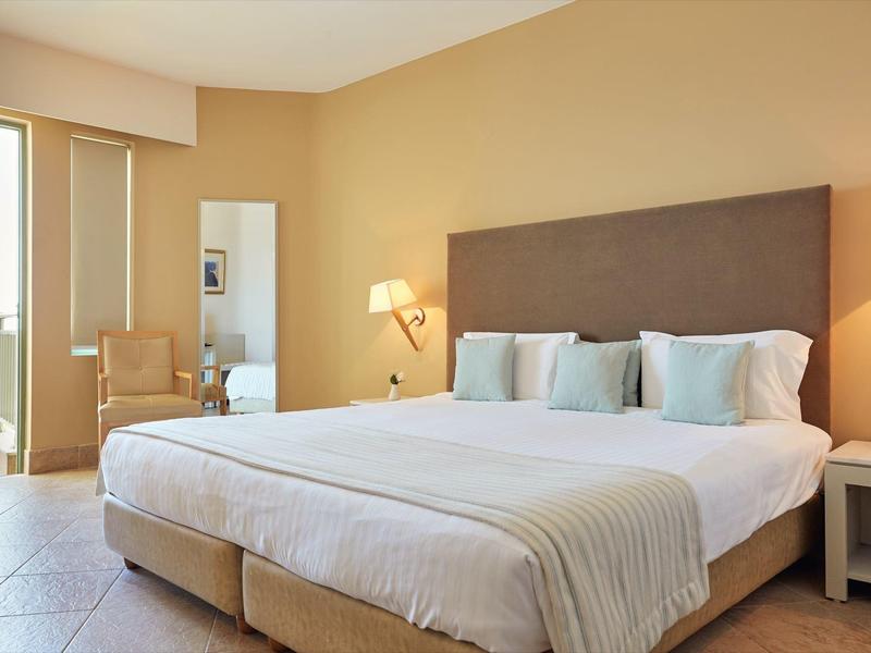 Camera d'hotel luminosa con letto grande, comodini e sedia vicino alla finestra