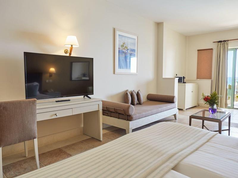 Camera d'albergo luminosa con letto matrimoniale, divano, scrivania, TV e balcone con vista.