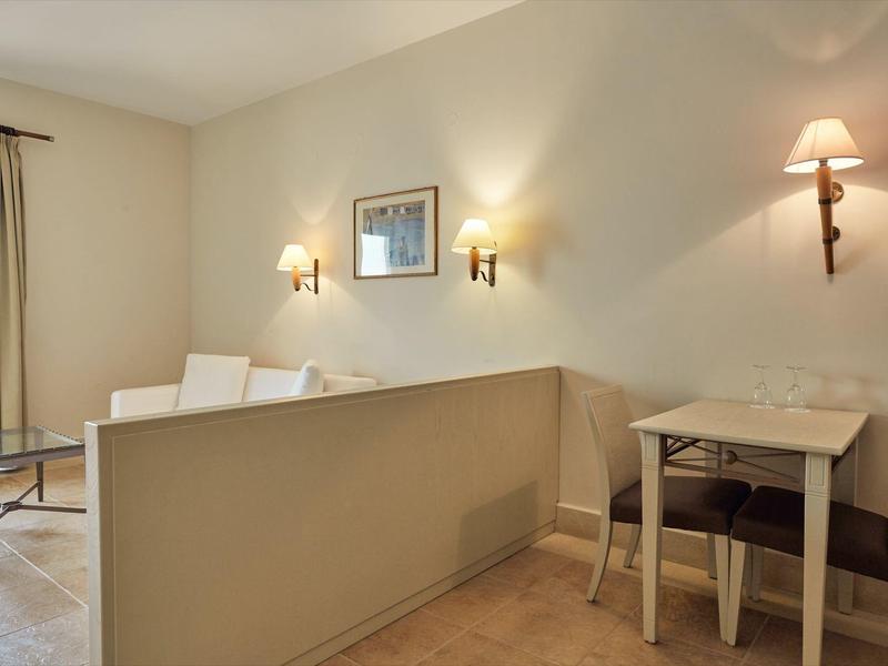 Accogliente camera d'hotel con divano, piccoli tavoli e lampade da parete in un ambiente luminoso.