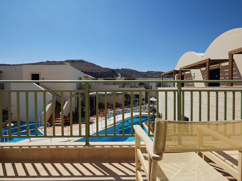 Vista da un balcone con sedia che domina una piscina e edifici circostanti sotto un cielo sereno
