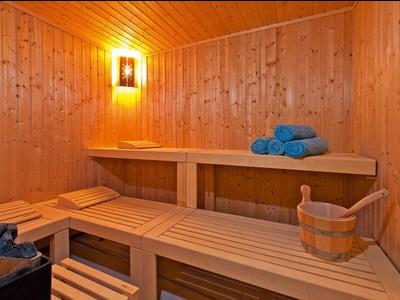 Sauna de madera con bancos en dos niveles, cubo de madera y toallas azules bajo luz cálida.