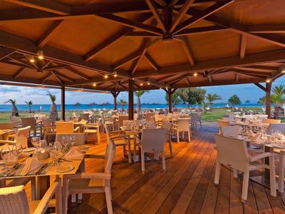 Restaurante abierto con suelo de madera y vista al mar al atardecer.