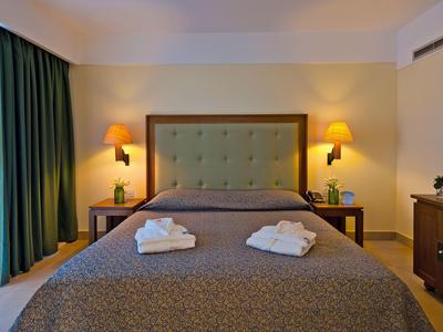 Habitación de hotel acogedora con cama grande, dos pilas de toallas y luz cálida.