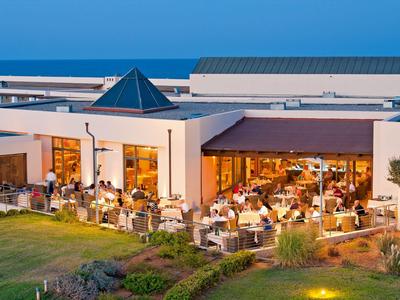 Beleuchtetes Restaurant im Freien eines Hotels bei Abenddämmerung mit Gästen und grünem Garten.