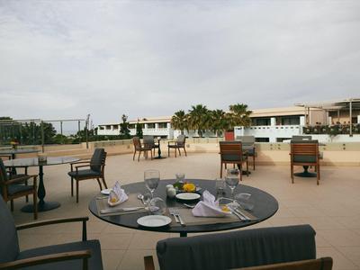 Eine Dachterrasse mit mehreren Tischen und Stühlen, gedeckt für ein Essen, mit Blick auf Gebäude und Palmen.