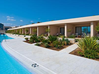 Moderner Hotelkomplex mit langem Pool und grünen Pflanzen unter klarem blauem Himmel.