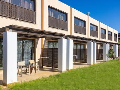 Filas de habitaciones de hotel con verandas y césped en primer plano bajo cielo despejado.
