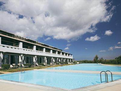 Complejo hotelero moderno con gran piscina al aire libre bajo cielo azul con nubes blancas.
