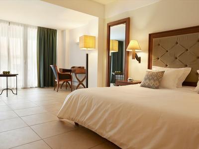 Habitación de hotel luminosa con cama grande, escritorio, sillas y balcón con cortinas.