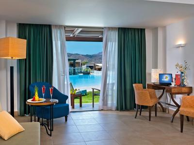 Sala con sillón azul, sillas amarillas, escritorio y vista a la piscina y montañas.