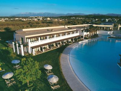 Großes Hotel mit Pool und Sonnenschirmen in einer sonnigen Landschaft.