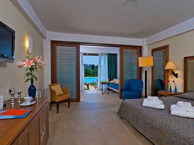 Habitación de hotel moderna con cama doble, terraza y vista al mar, iluminada cálidamente y decorada con estilo.