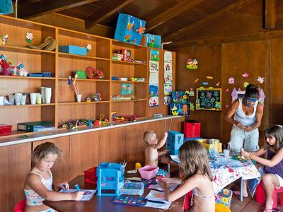 Niños y una cuidadora en una sala de juegos con estanterías llenas de juguetes y libros en un hotel.