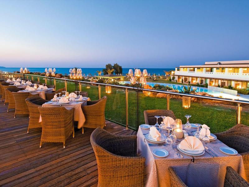 Terraza de restaurante con mesas preparadas, vista a la piscina y al mar al atardecer.