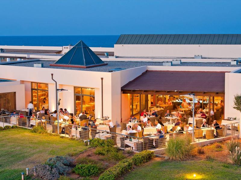 Área exterior de un restaurante al atardecer con huéspedes y arquitectura moderna en el hotel.