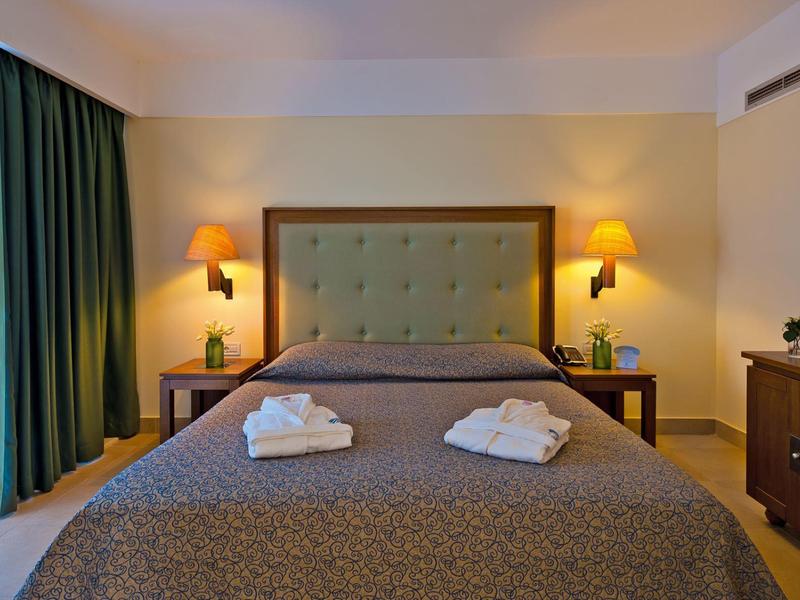 Habitación de hotel acogedora con cama grande, dos pilas de toallas y luz cálida.