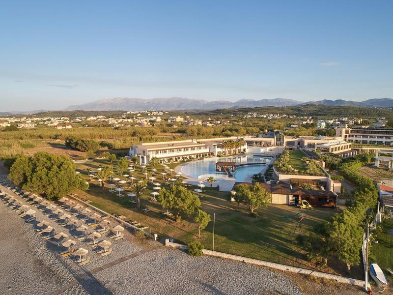 Resort vacacional con piscina, tumbonas, áreas verdes y montañas al fondo bajo cielo despejado.