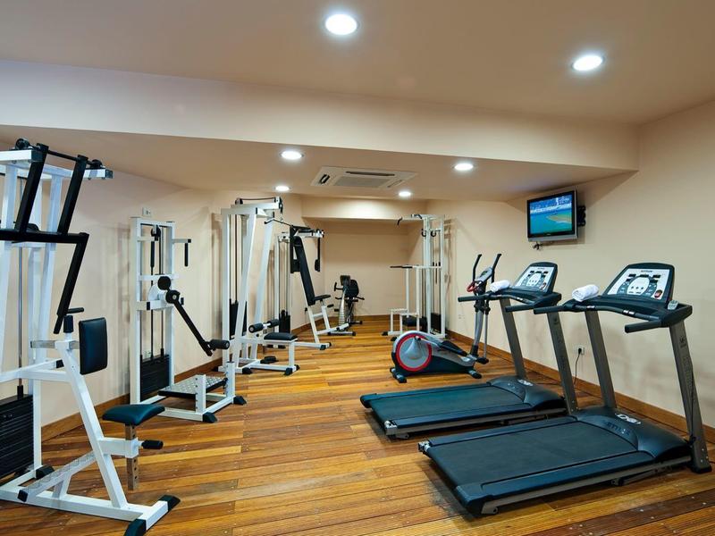 Gimnasio bien iluminado con suelo de madera, máquinas de entrenamiento y tres cintas de correr junto a la pared.