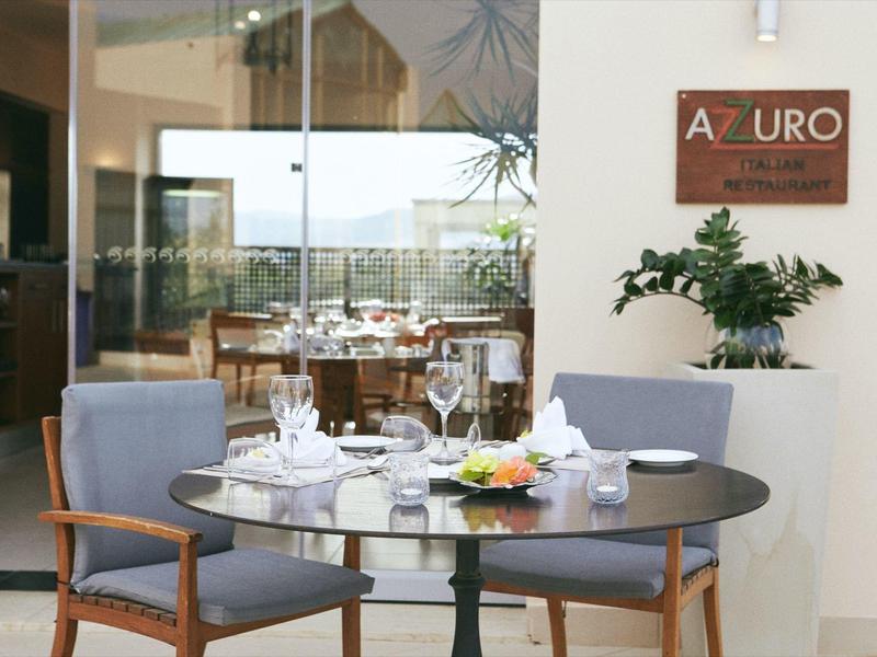 Una mesa de jardín preparada con sillas frente a ventanas de vidrio y vista a una terraza con montañas al fondo.
