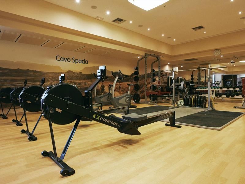 Gimnasio moderno con máquinas de remo y pesas sobre suelo de madera clara.