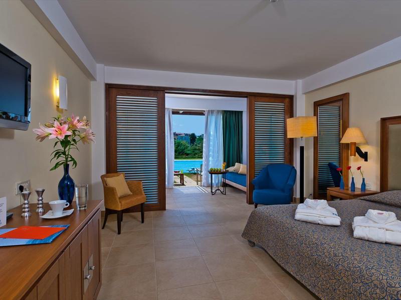 Habitación de hotel moderna con cama doble, terraza y vista al mar, iluminada cálidamente y decorada con estilo.