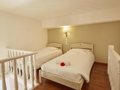 Gemütliches helles Schlafzimmer mit zwei Einzelbetten, holzfarbenem Boden und moderner Wandbeleuchtung.