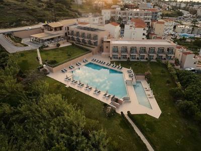 Großes Hotel mit Pool, Sonnenliegen und grüner Landschaft, umgeben von Hügeln und Häusern.