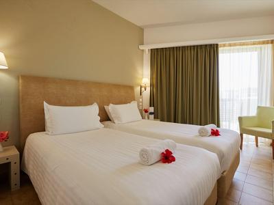 Hotelzimmer mit zwei Einzelbetten, weißen Bettwäsche, Blumen und Balkon.