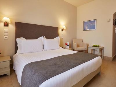 Helles Schlafzimmer mit großem Bett, grauer Bettdecke, Sessel, Nachttisch und Wandlampen.