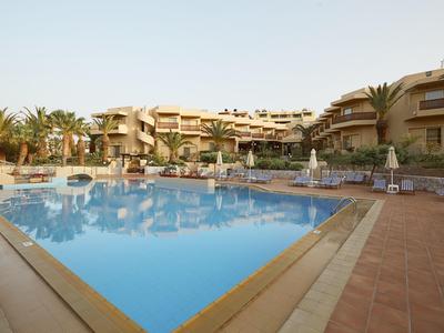 Hotel mit blauem Pool, Sonnenschirmen und Palmen unter klarem Himmel.
