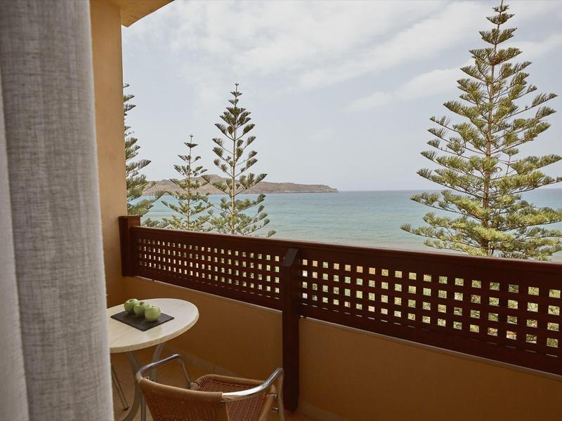 Balcón con silla y mesa, vista al mar y pinos altos bajo un cielo nublado.