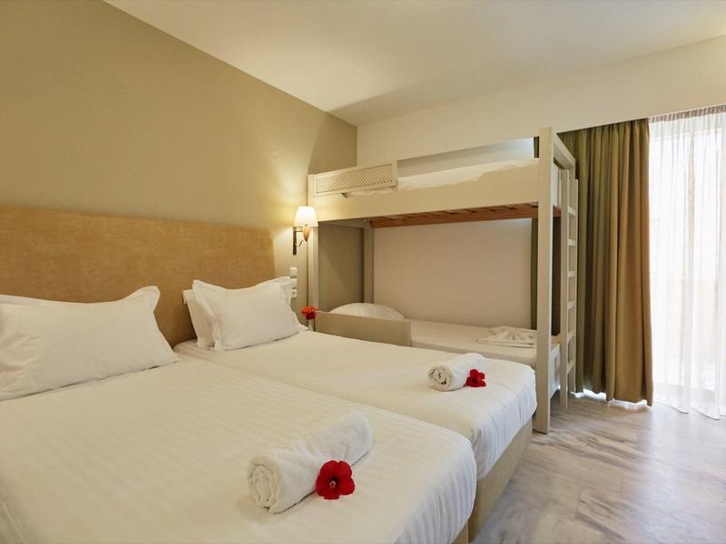 Habitación de hotel con cama doble, litera, cortinas y suelo de madera clara.